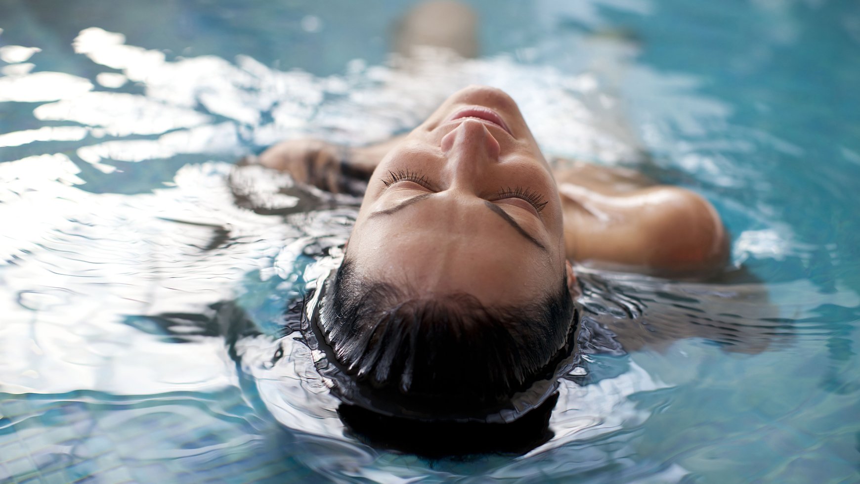 A person lays in the pool with head half submerged, looking very relaxed on a spa day at Warner Hotels