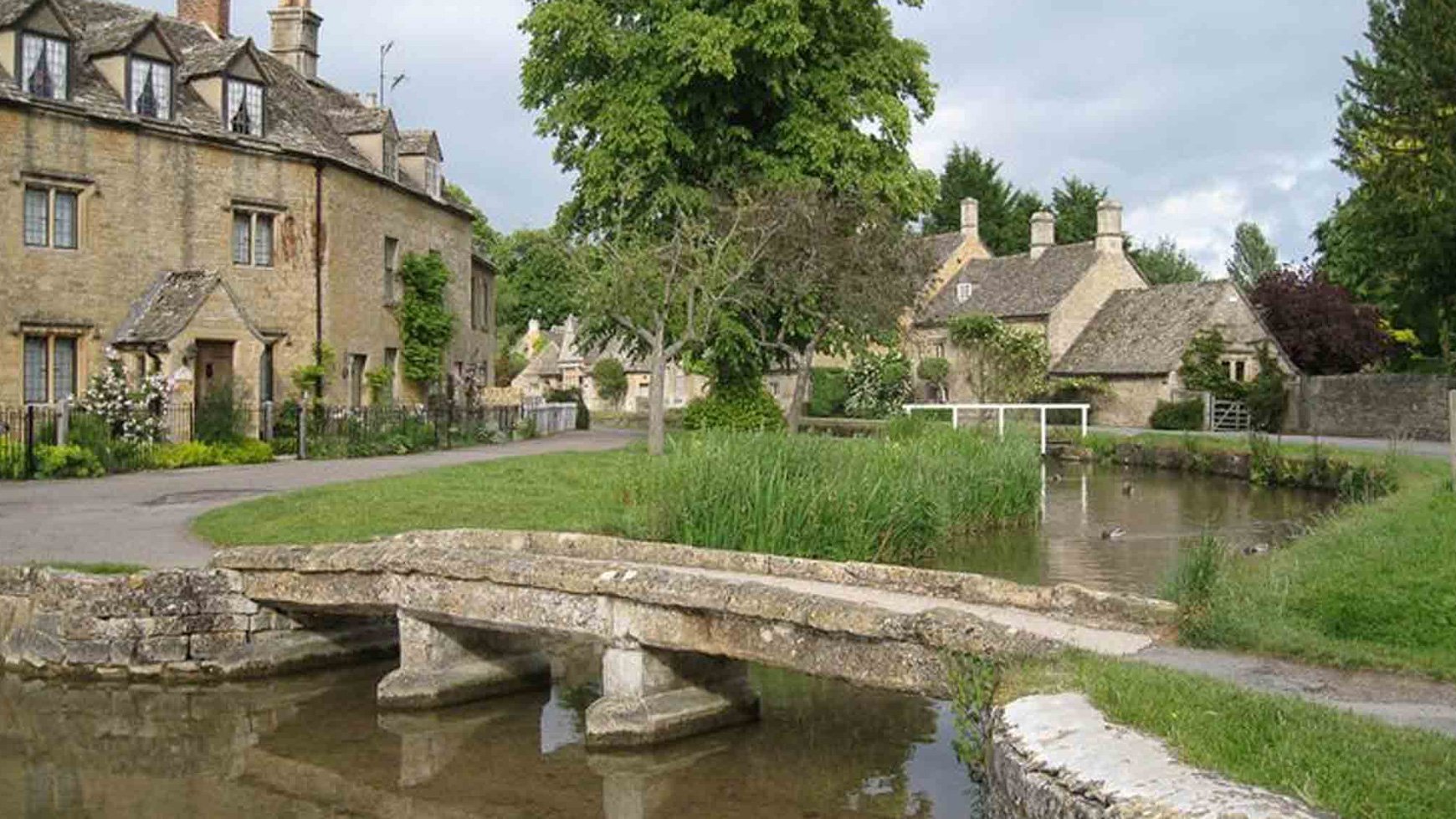 A charming stone bridge crosses a river in Bourton-on-the-Water, a scenic village in the Cotswolds, West Midlands.